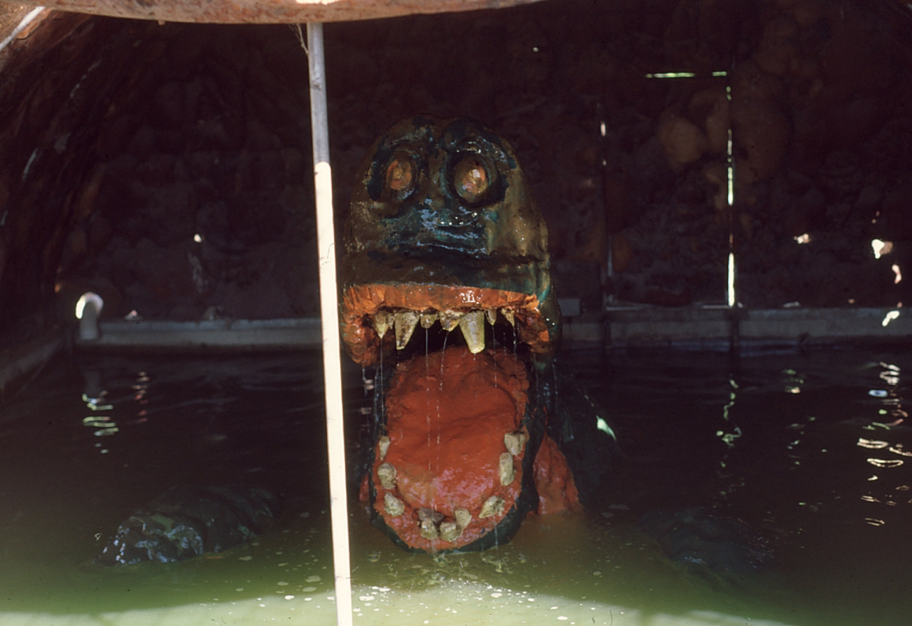 a green-colored sea monster animatronic, lizardlike in appearance with an open mouth, sunken into water