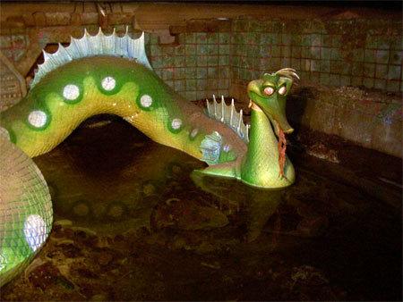 a sea serpent animatronic, green in coloration, with a snout like a seahorse. its noodle-like body sits in putrid water
